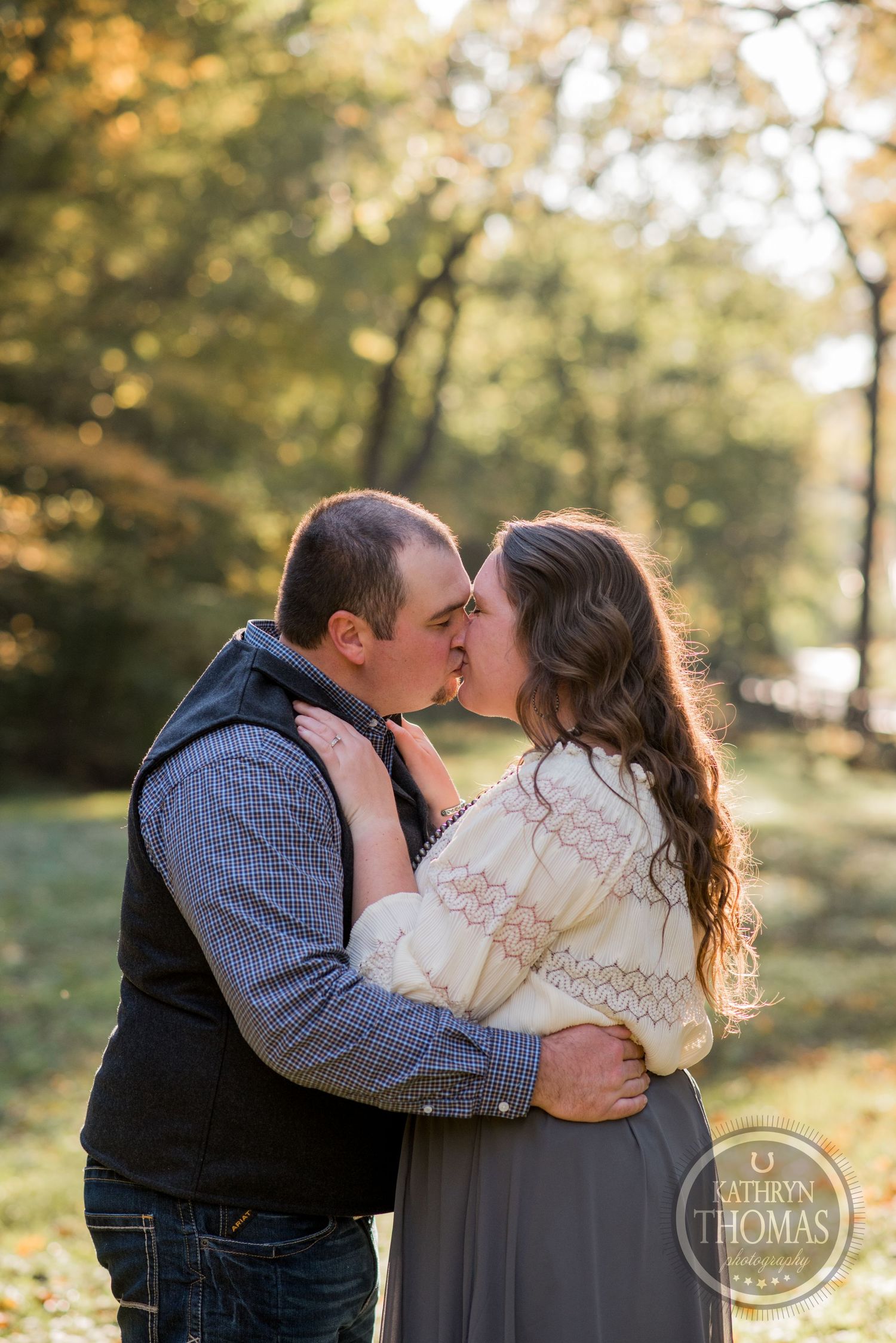 An intimate moment captured between a couple in casual attire against a sun-lit autumn forest background.