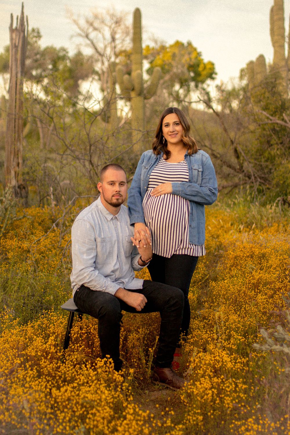 A couple poses together amidst blooming yellow wildflowers and saguaro cacti in the desert.