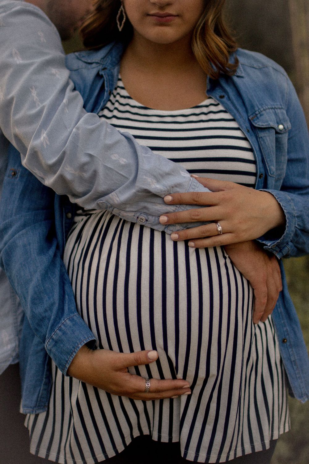 Close-up of hands cradling a pregnant belly in striped dress and denim jacket.