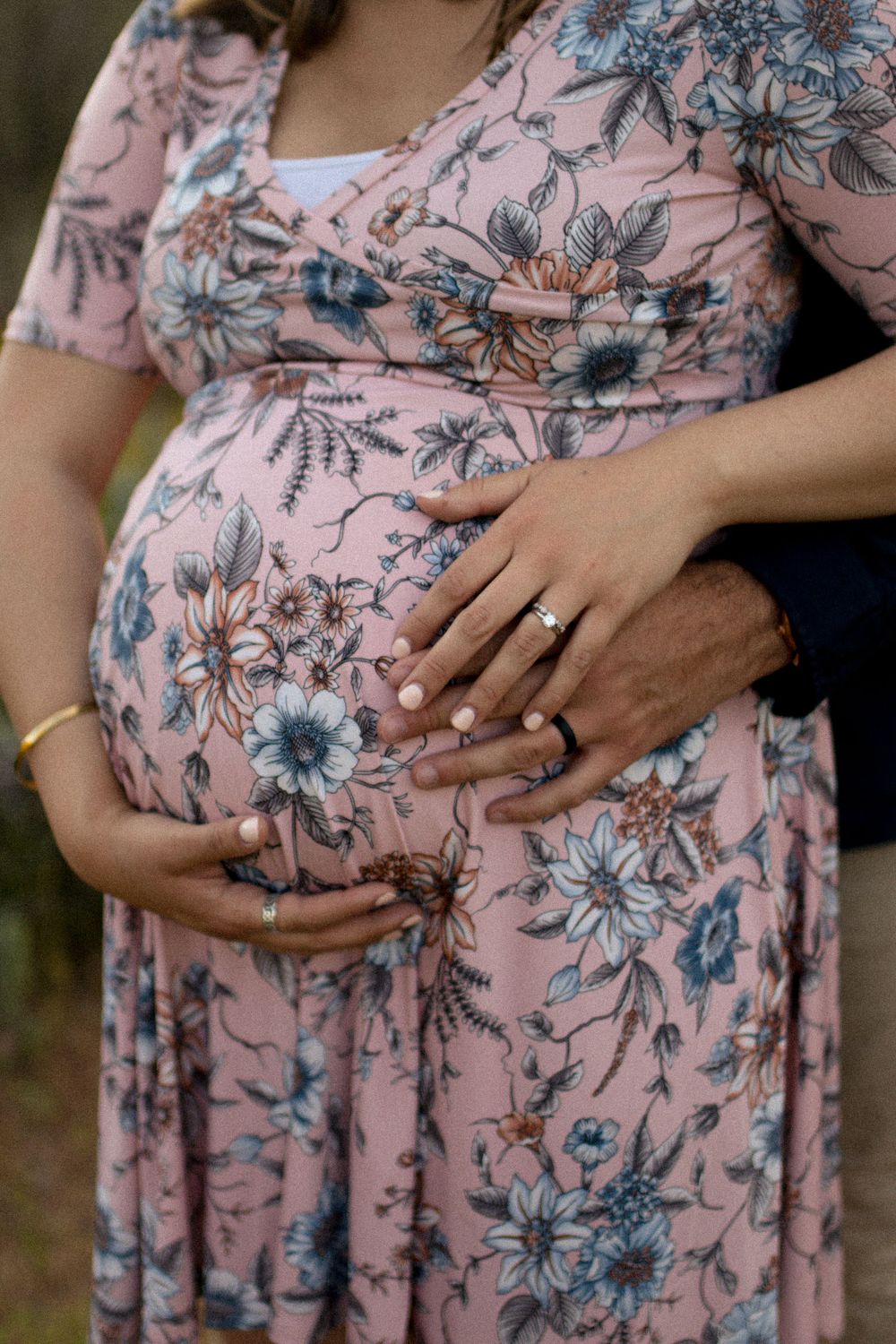 Close-up detail of hands cradling baby bump in pink floral maternity dress.