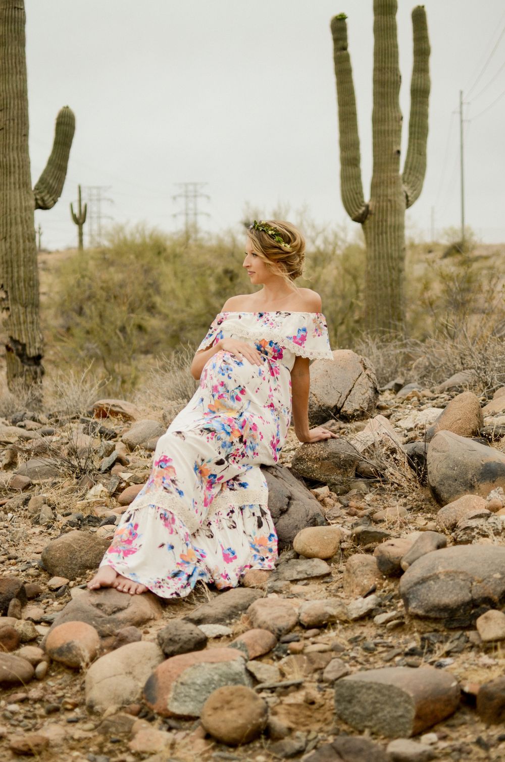 Woman in floral dress poses among rocks and saguaro cacti in desert landscape.