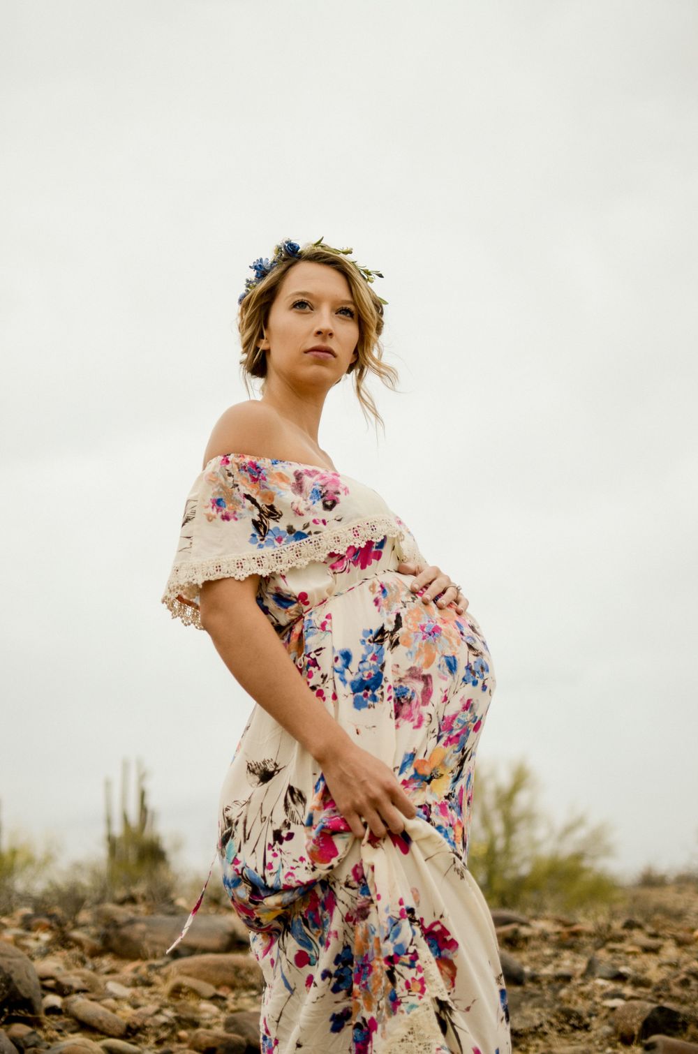Desert maternity photoshoot featuring a floral maxi dress and dramatic cloudy sky.