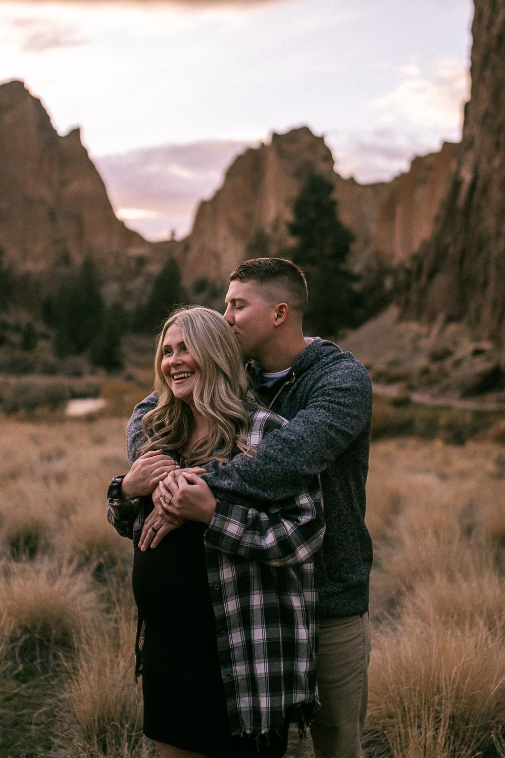 Couple embracing in front of majestic rock formations during sunset photo session.