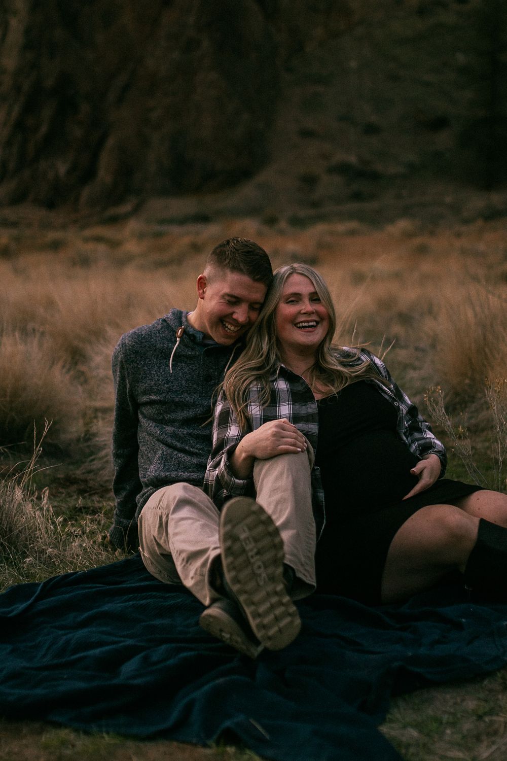 Couple sharing laughter while sitting on blanket against rocky landscape backdrop.