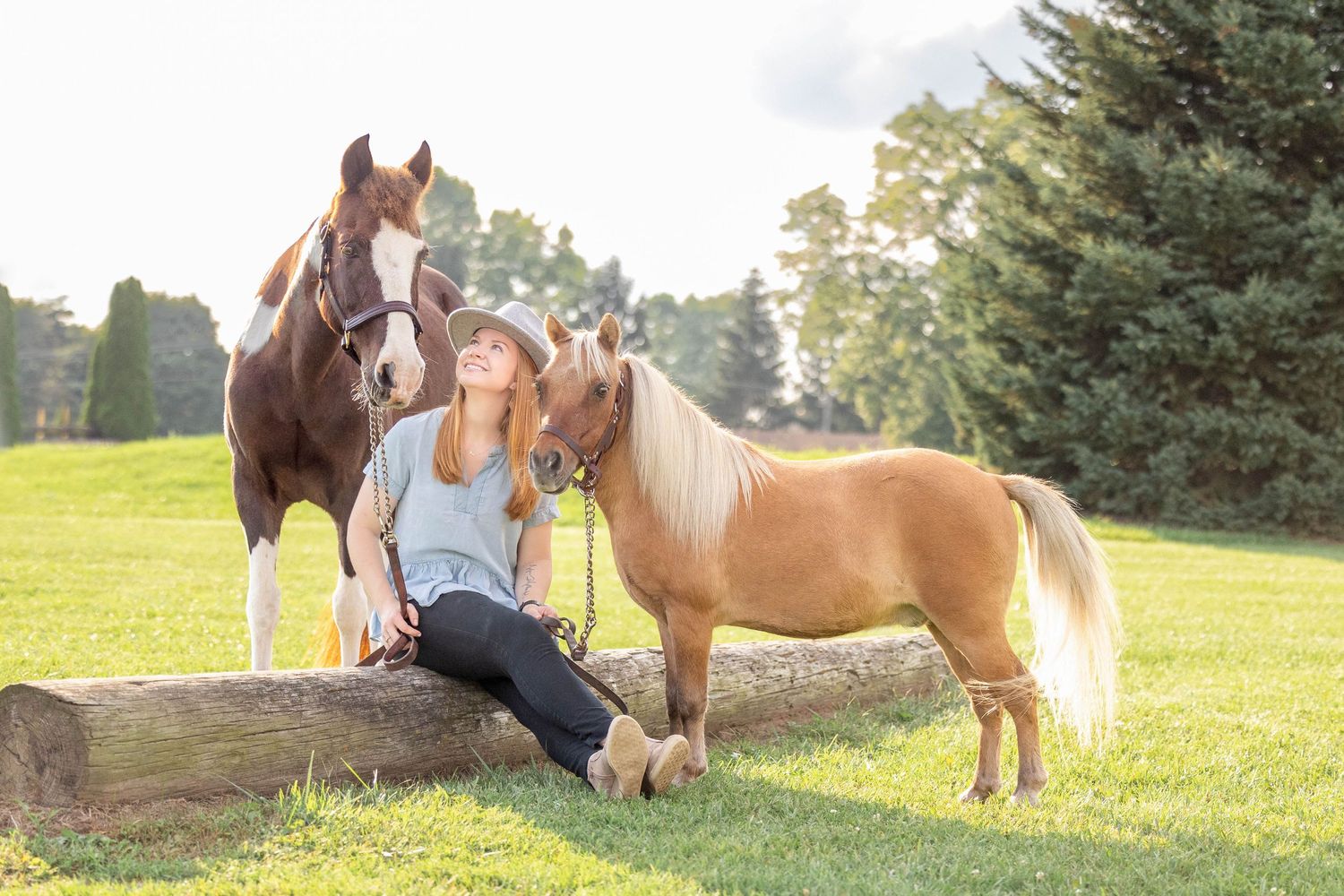 Emily sitting on a log while holding her paint pony and mini
