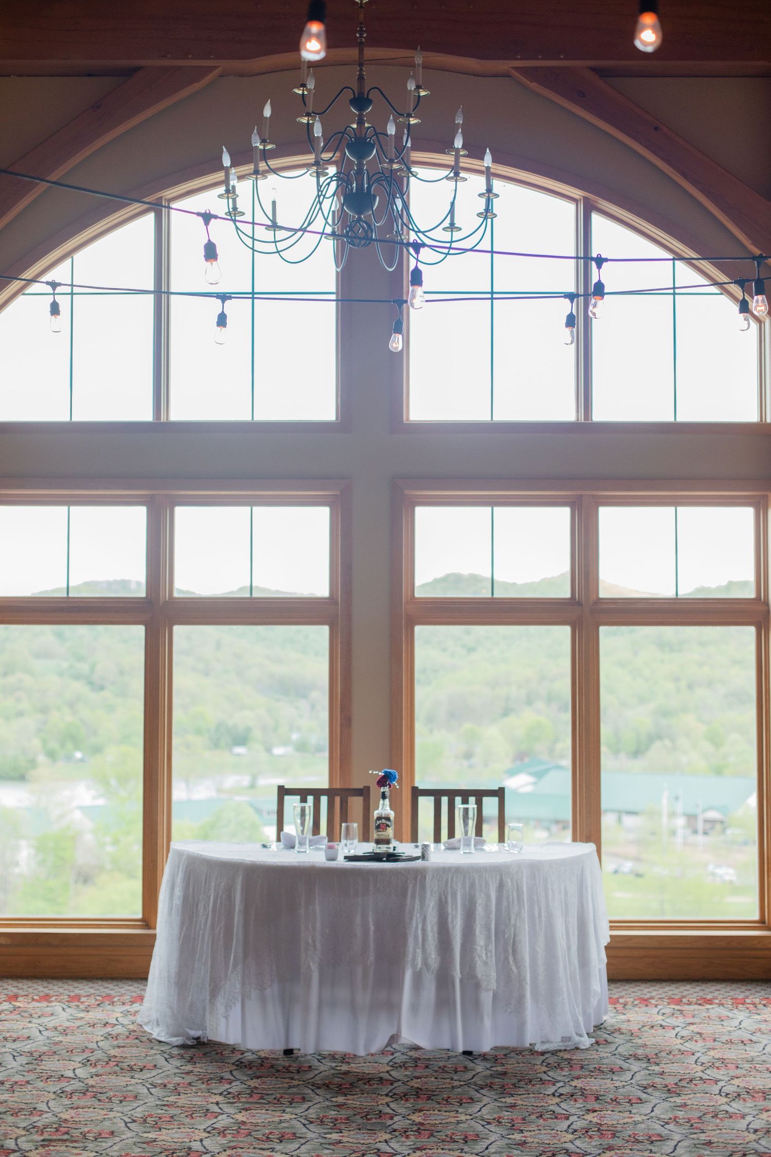 Elegant wedding venue interior with arched windows, chandeliers and round tables with white linens.