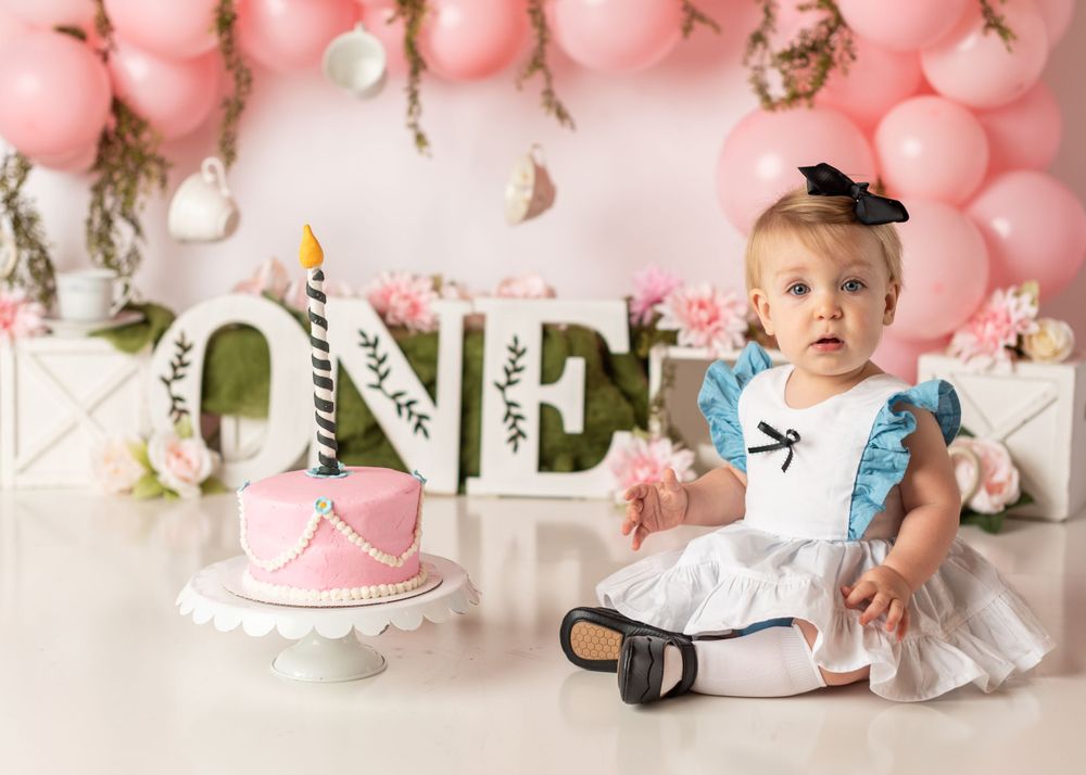 First birthday cake smash setup with pink balloons and 'ONE' letters as decorative backdrop.