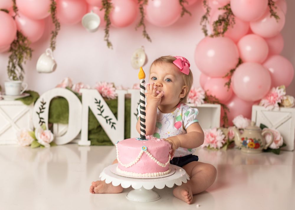 Birthday cake smash session with pink balloon arch and floral decorations.