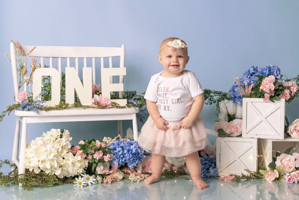 Floral first birthday setup with white bench, roses, and decorative 'ONE' letters.