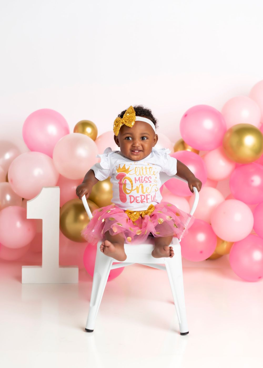 Pink and gold balloon backdrop with number one for first birthday celebration.