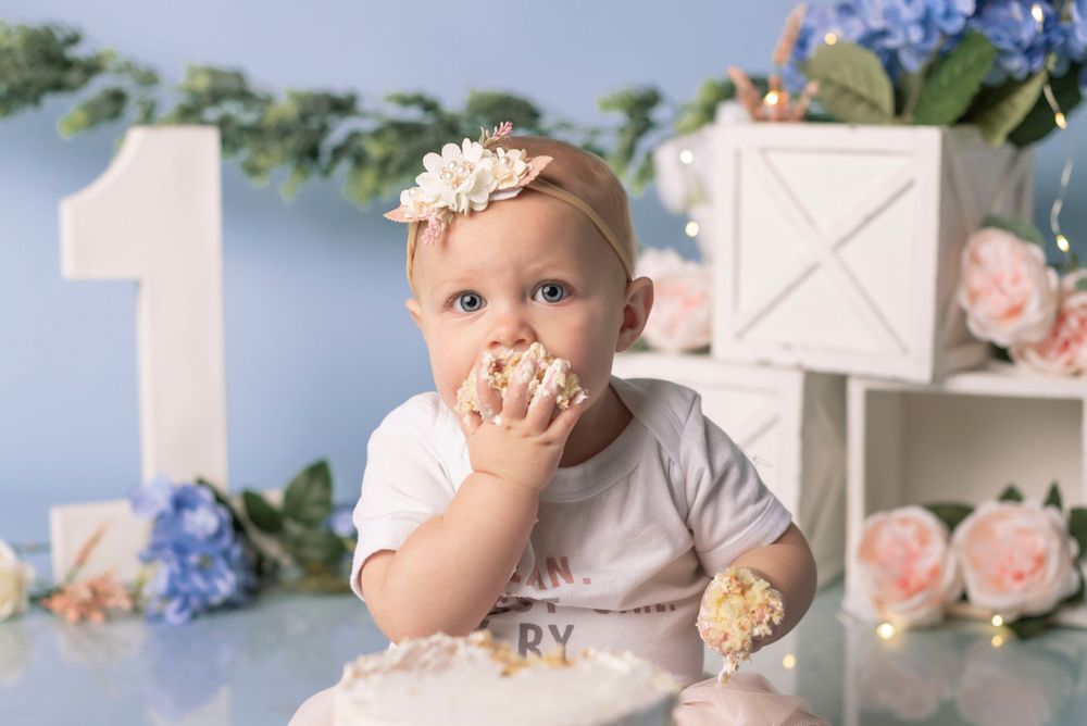 Delicate floral first birthday setup with blue and pink flowers against a pale blue backdrop.