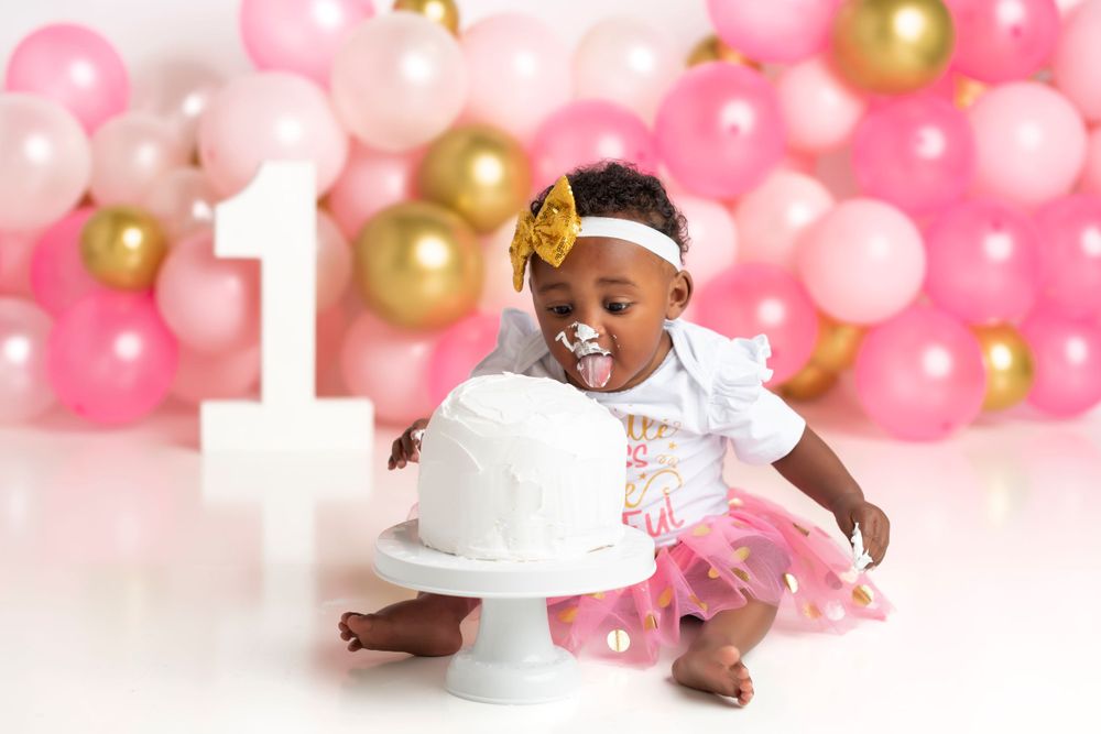 First birthday setup with pink and gold balloons and white cake stand.
