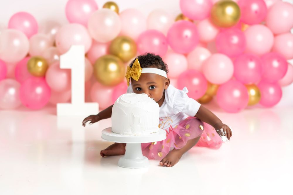 Pink and gold balloon backdrop with white cake stand for first birthday photoshoot.