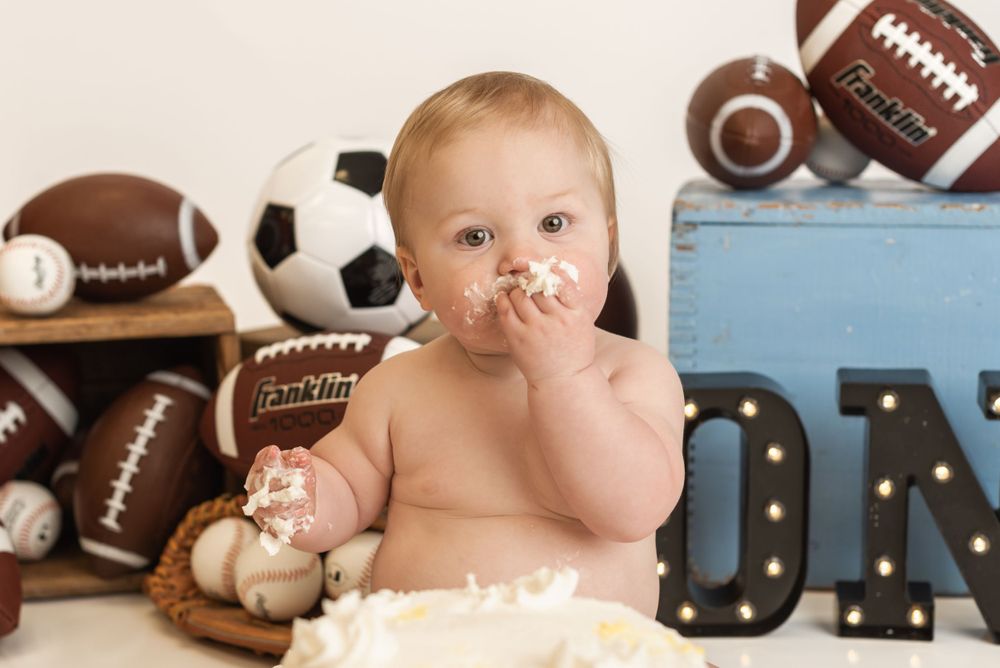 Cake smash photo with sports equipment and blue letters in the background.