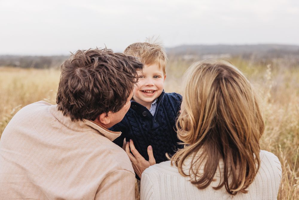 A sweet family interaction captured in a sunny field with mountains in the background.