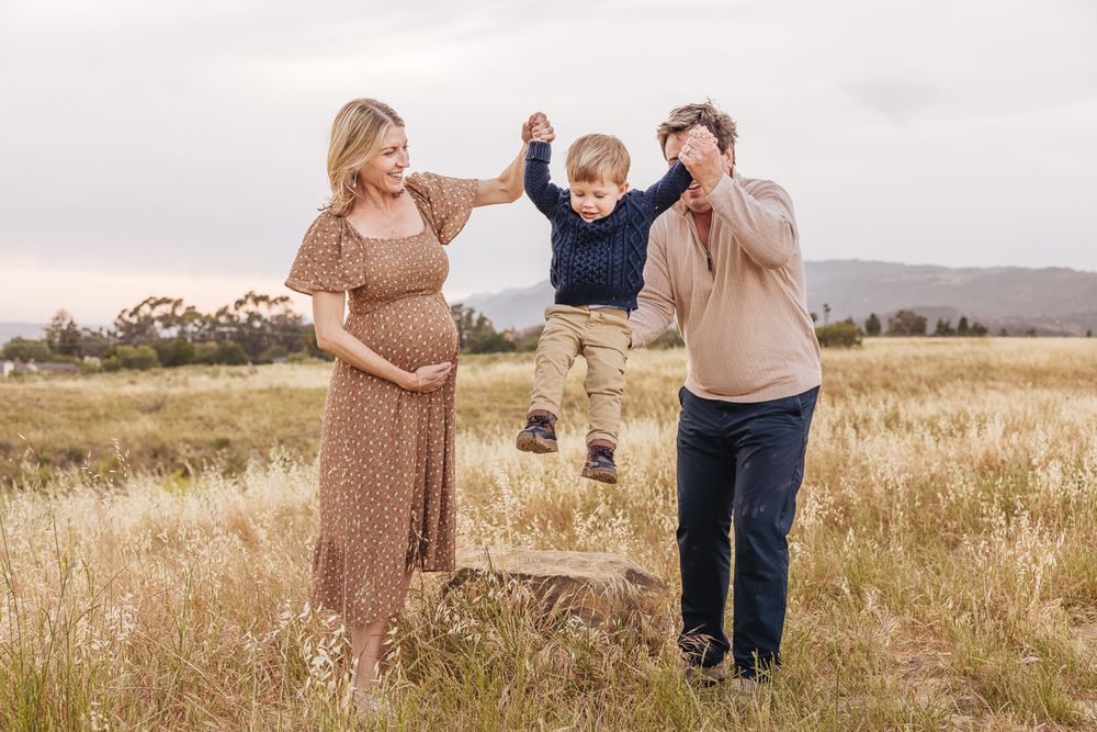 A playful family moment in a golden field with mountains behind them.