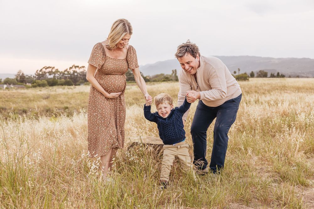 A happy family holding hands and playing in a golden field with mountains in the background.