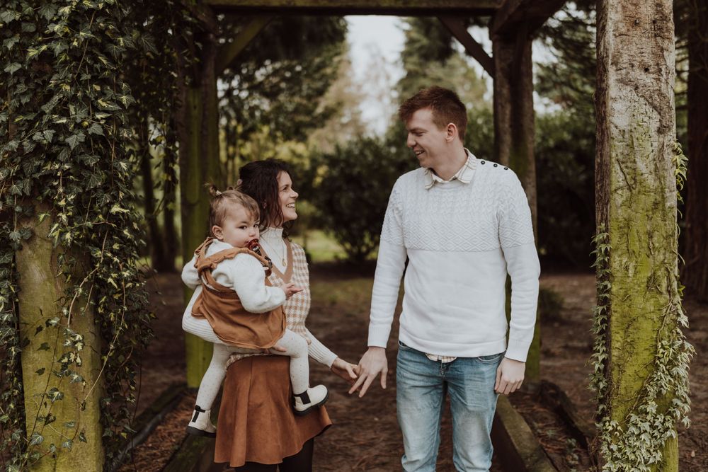 Family walking together under rustic wooden garden arch covered in green moss.