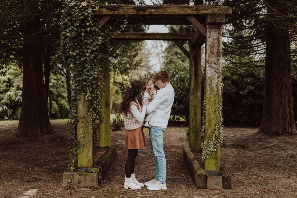 A couple embraces under a moss-covered wooden archway in a forest setting.