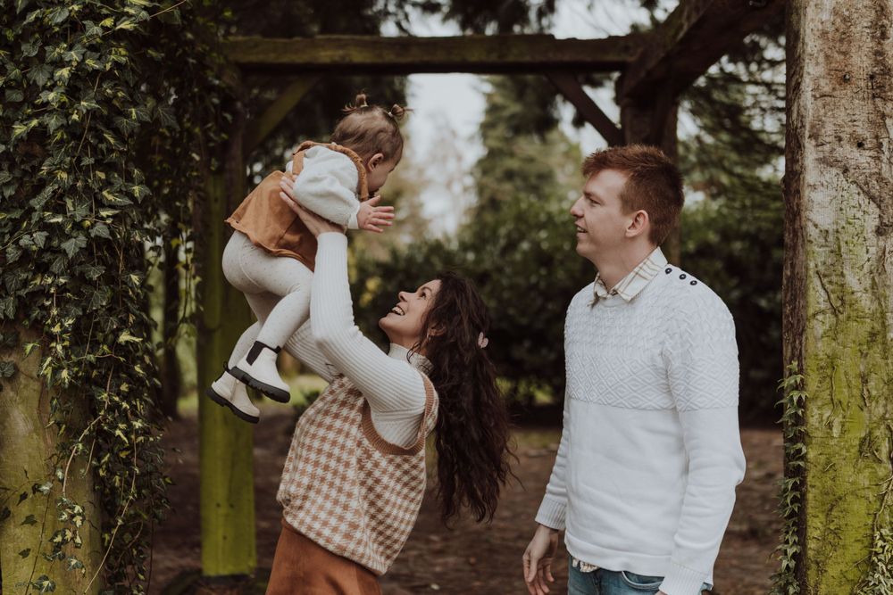 Touching family moment captured in a garden archway with greenery and moss on warm autumn day.