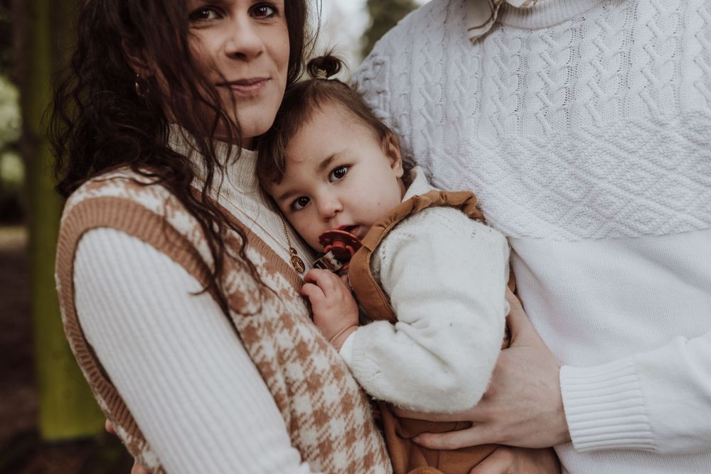 Close-up family portrait under wooden pergola showing tender moment.