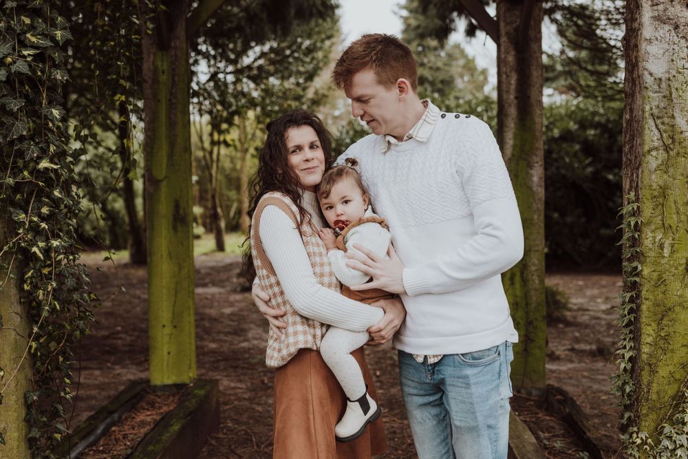 Casual family portrait under rustic wooden pergola in natural outdoor setting.