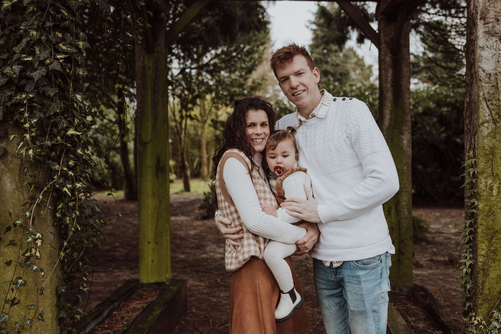 Family portrait under wooden archway in forest setting with matching casual attire.