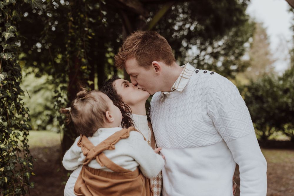 Sweet family moment shared under wooden garden archway surrounded by greenery.