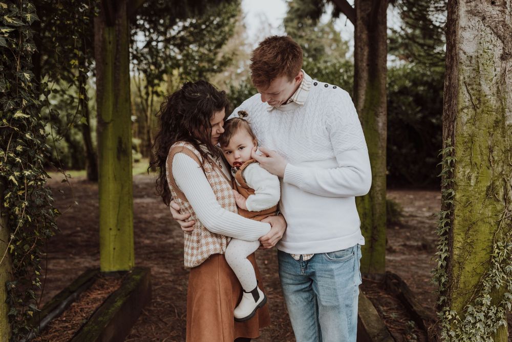 Intimate family moment captured under moss-covered wooden archway in forest.