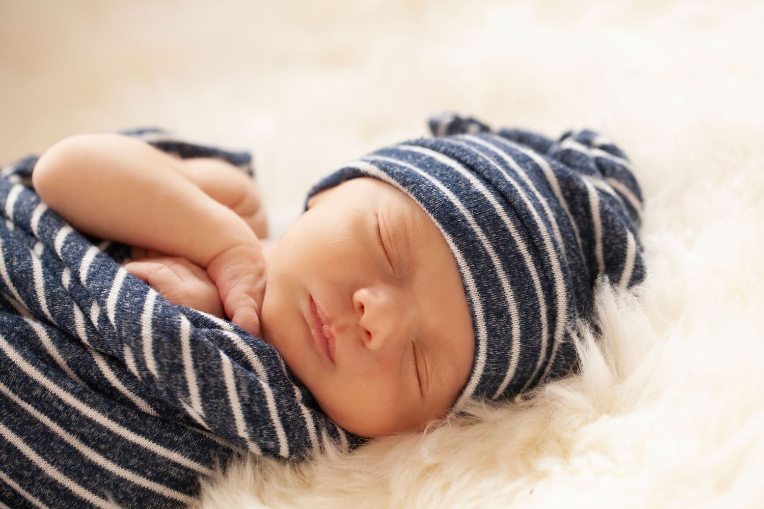 A sleeping newborn in striped clothing rests peacefully on white fur.