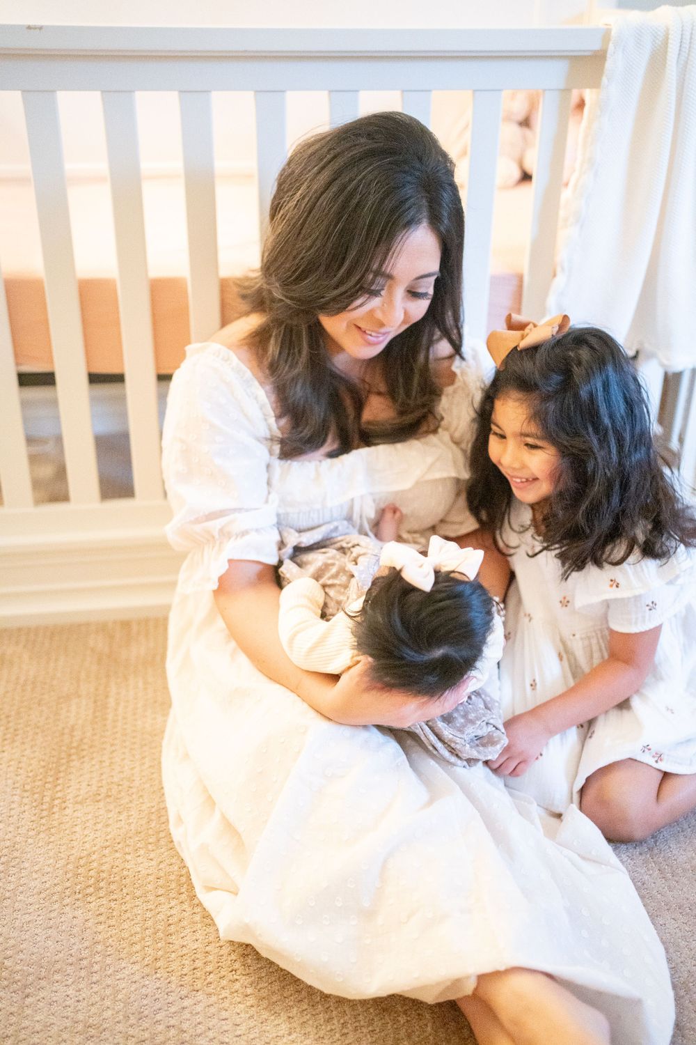 A tender family moment captured in white as mother and children share joyful laughter together on a carpeted floor.