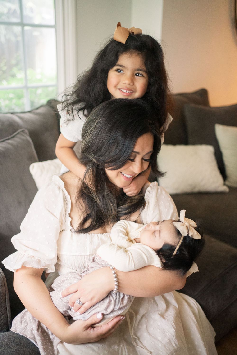 A tender moment of bonding on a couch as a child leans over while an infant is being cradled in soft natural light.