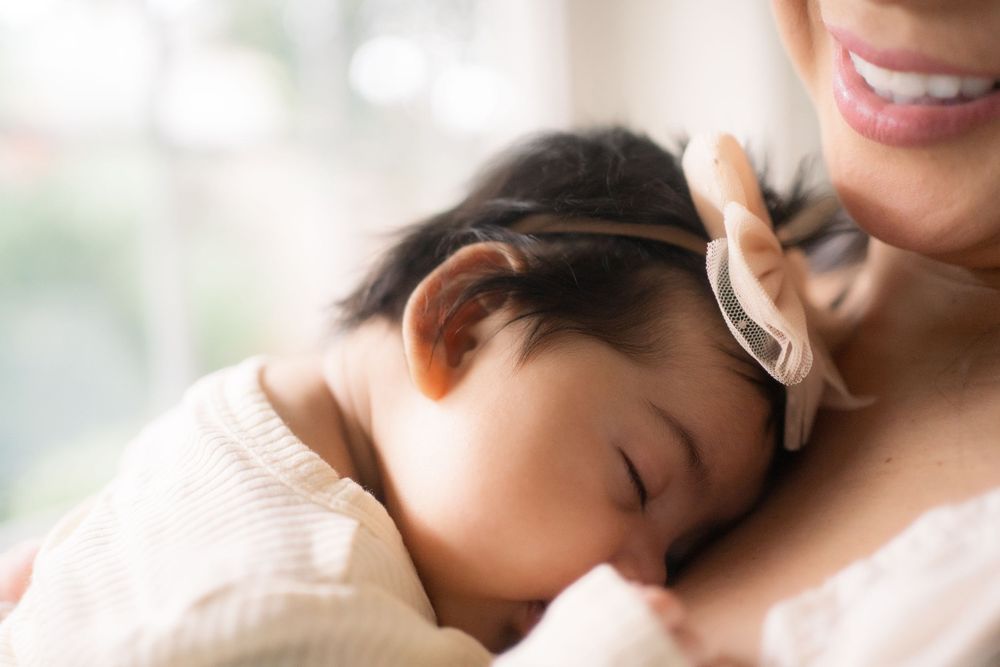 Baby sleeping peacefully while nestled close to parent in a tender embrace near window light.
