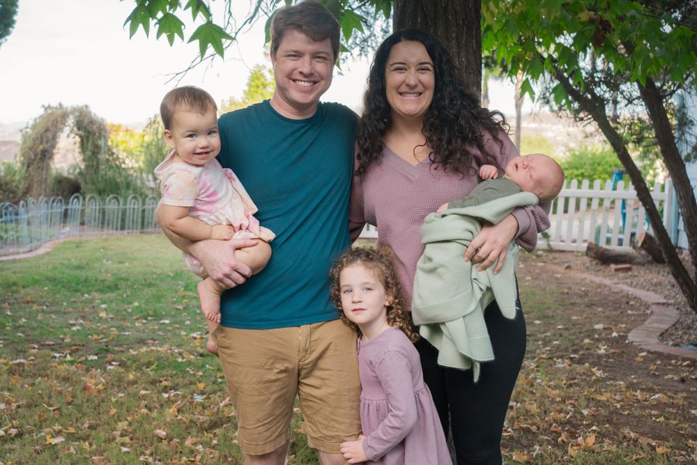 A family poses together outdoors in a backyard setting with autumn leaves on the ground.