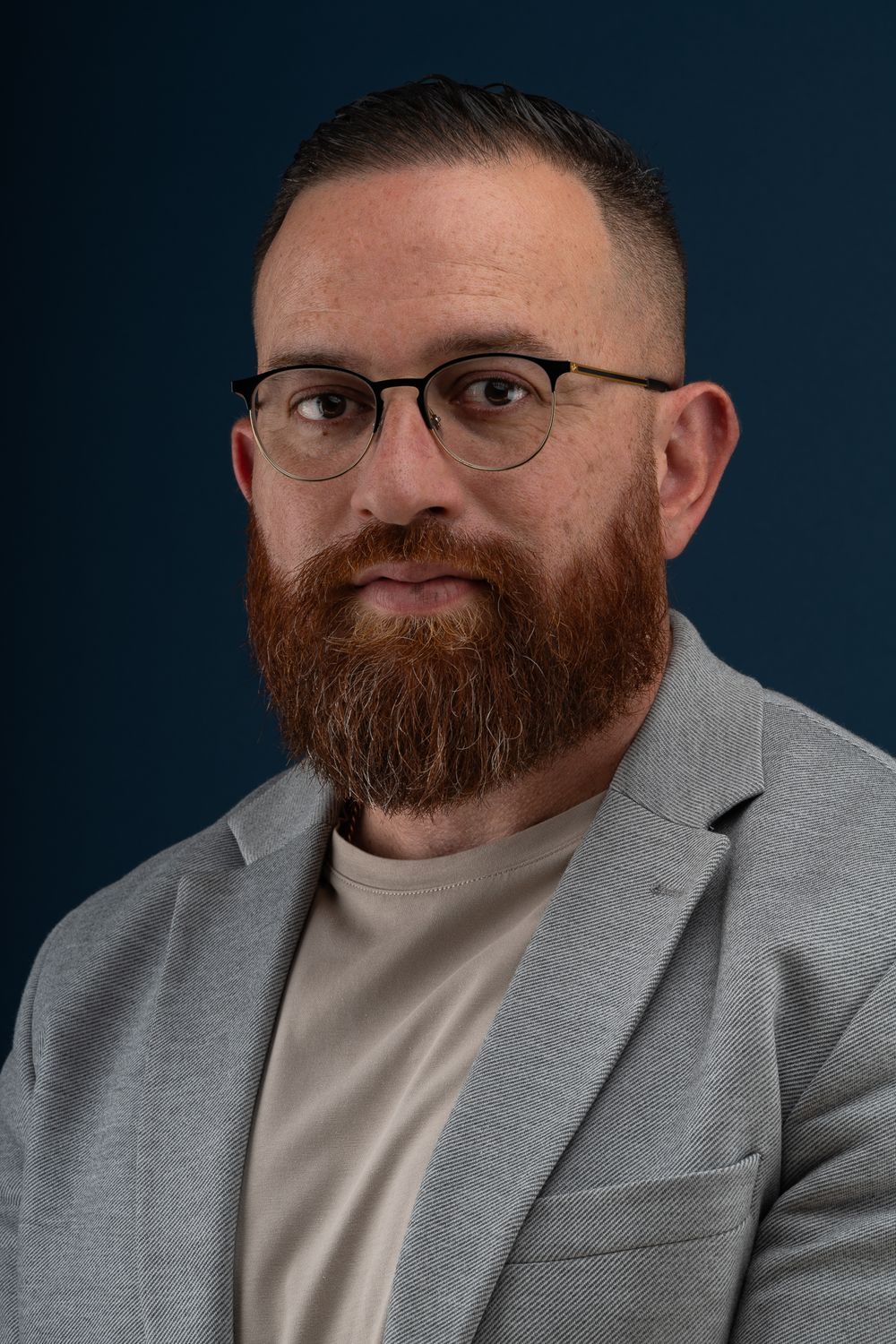 Close up portrait of person in grey blazer and glasses with full beard.