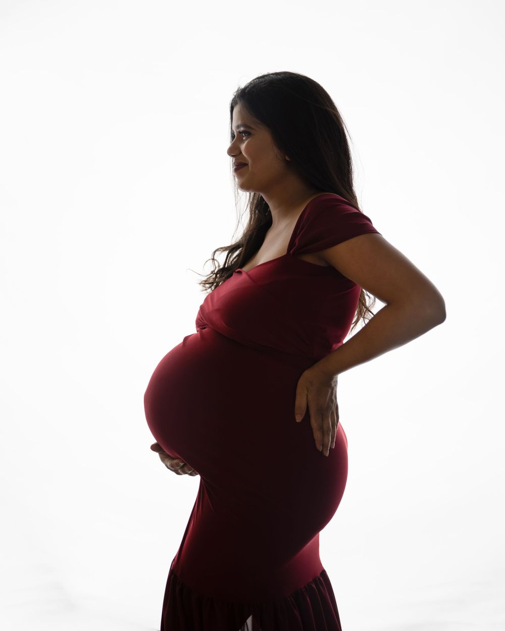 Silhouette of pregnant woman in red dress against white background.