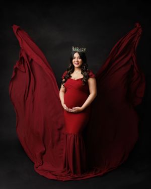 A maternity portrait with billowing burgundy fabric creating wing-like effect against dark backdrop.