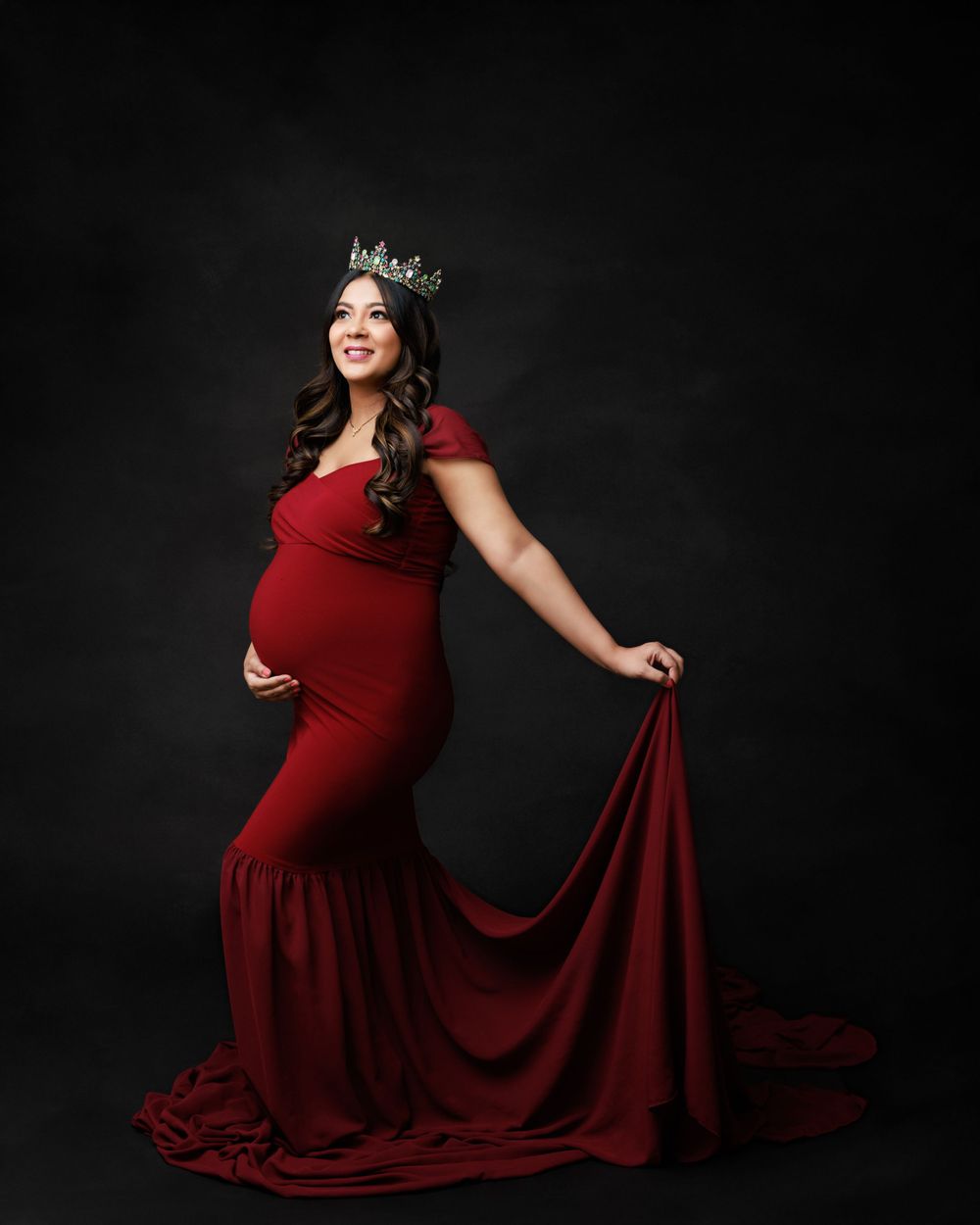 A maternity photo featuring a fitted red gown with dramatic train against dark background.