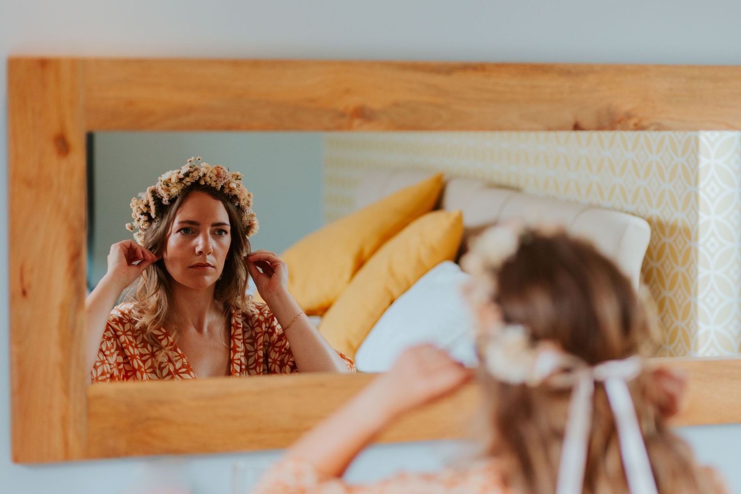 A reflection of a person wearing a floral crown in a wooden-framed mirror during wedding preparations.
