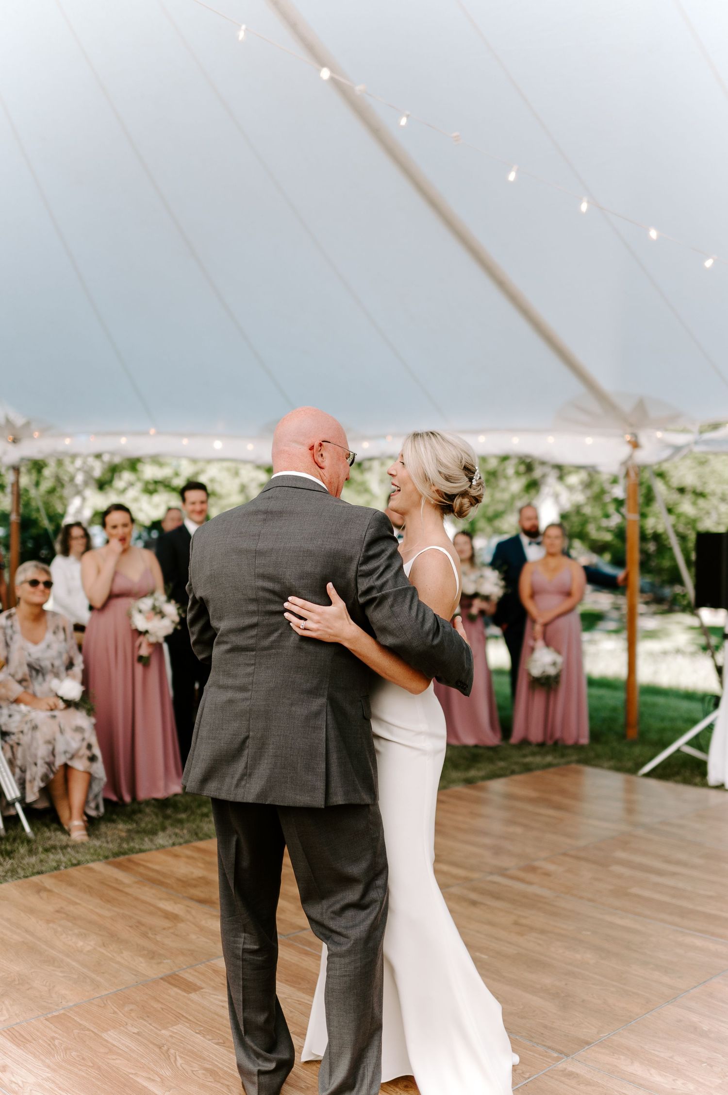 Wedding guests gather around dance floor to watch couple's special moment under tent.