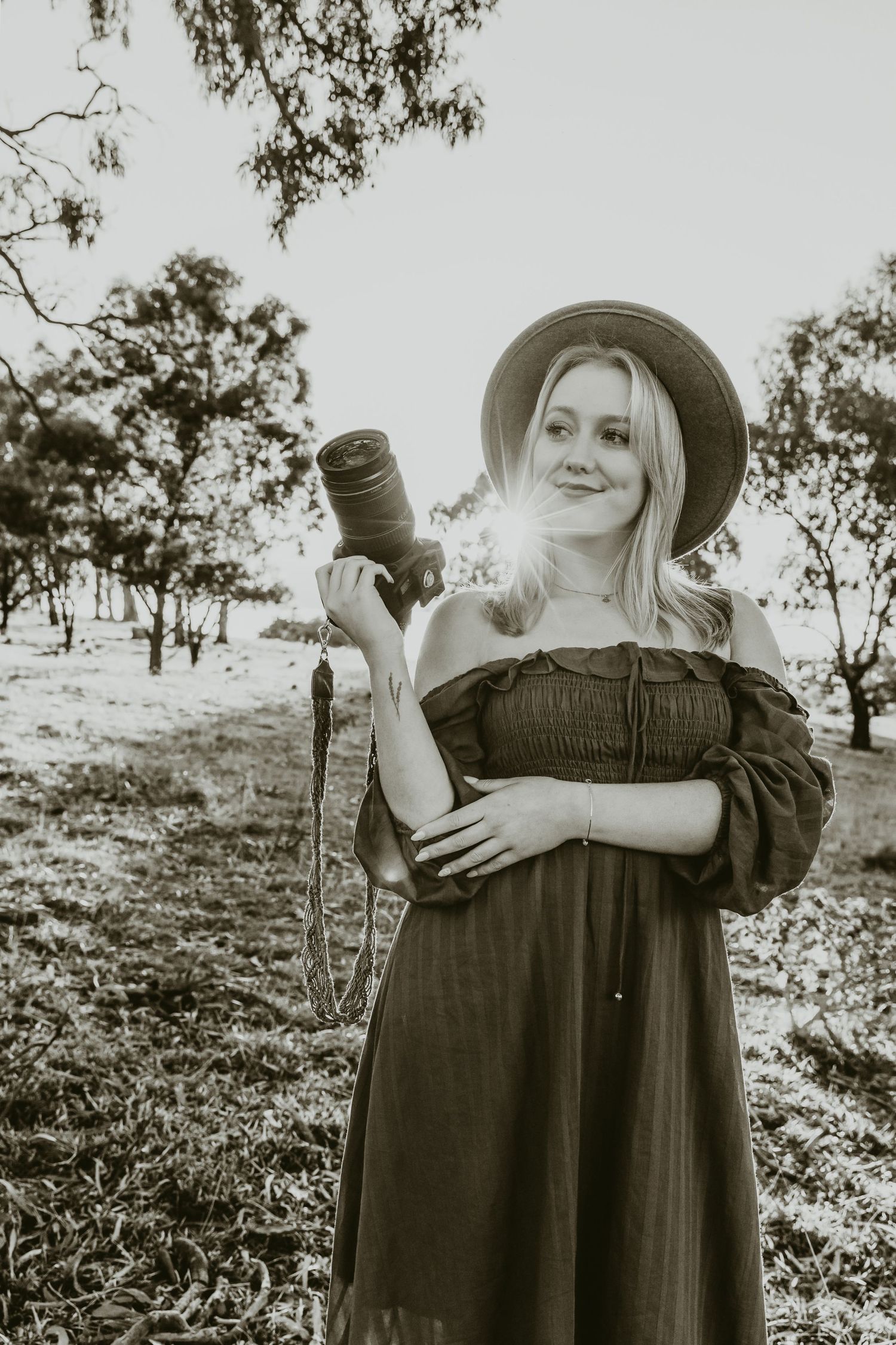 Black and white portrait of a photographer in a sun hat holding camera equipment outdoors.