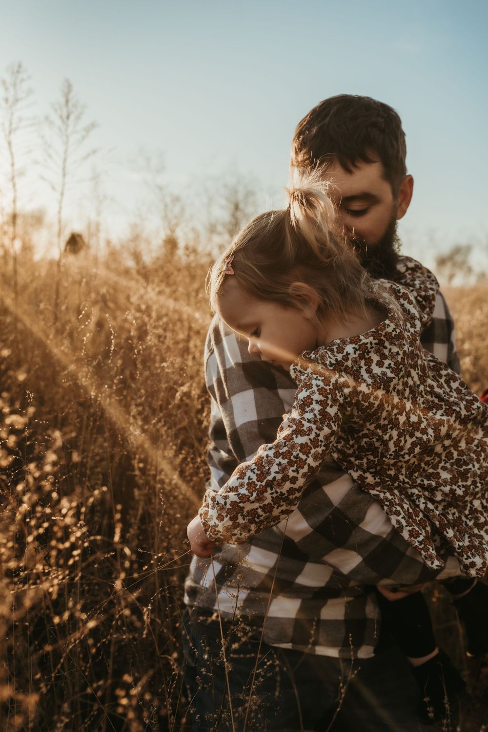 Tender family embrace captured during golden sunset in a field of dried grass.