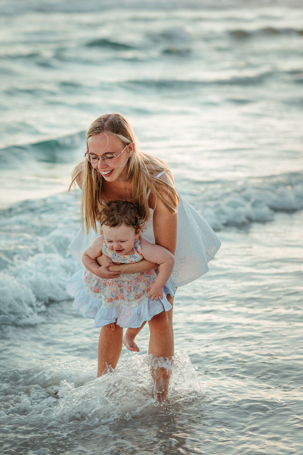 Parent and child splashing and playing in ocean waves during golden hour.