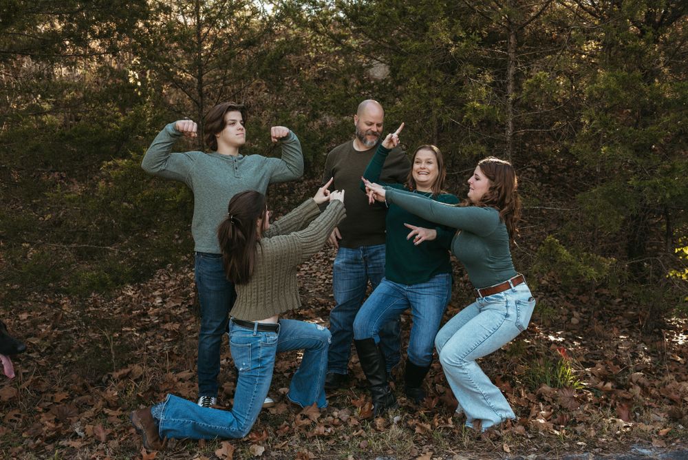 A playful group strikes silly poses together in an autumn forest setting at sunset.