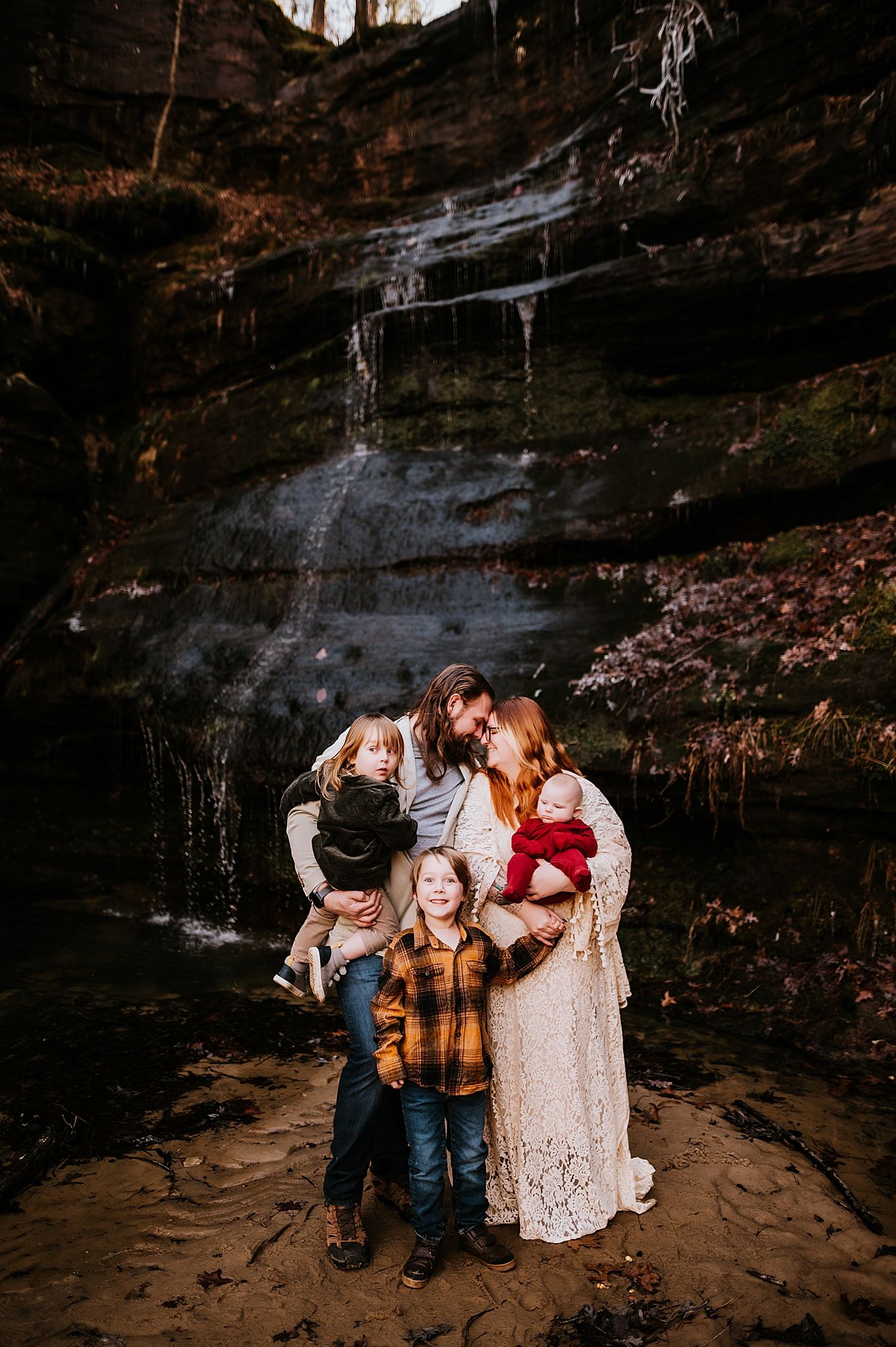 A family poses together in front of a scenic waterfall cascading down rocky cliffs.