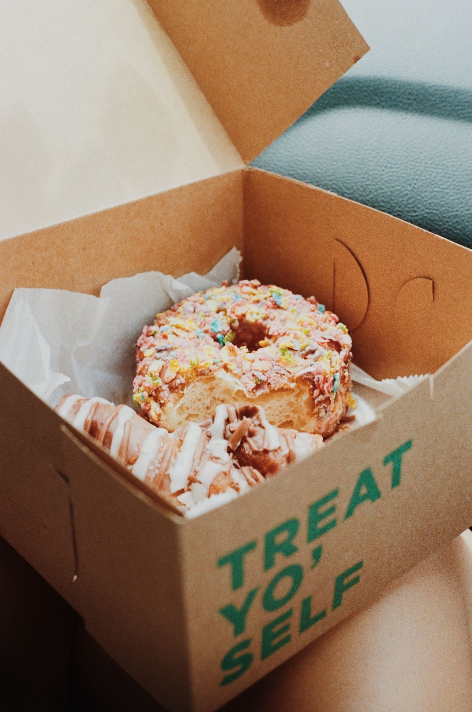 Fresh donuts with colorful sprinkles displayed in a cardboard takeout box.