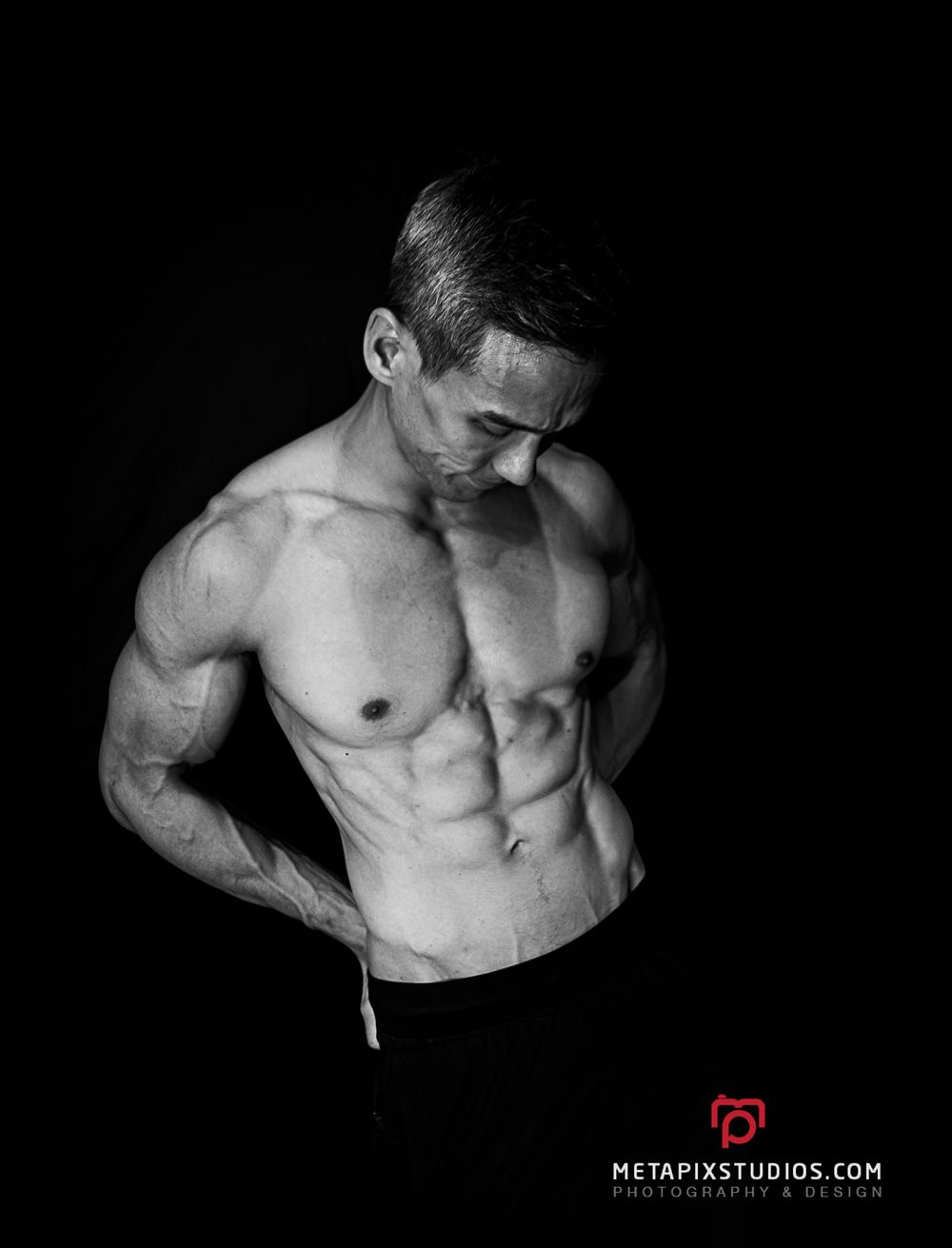Black and white image of a muscular shirtless man flexing his abs against a dark background.