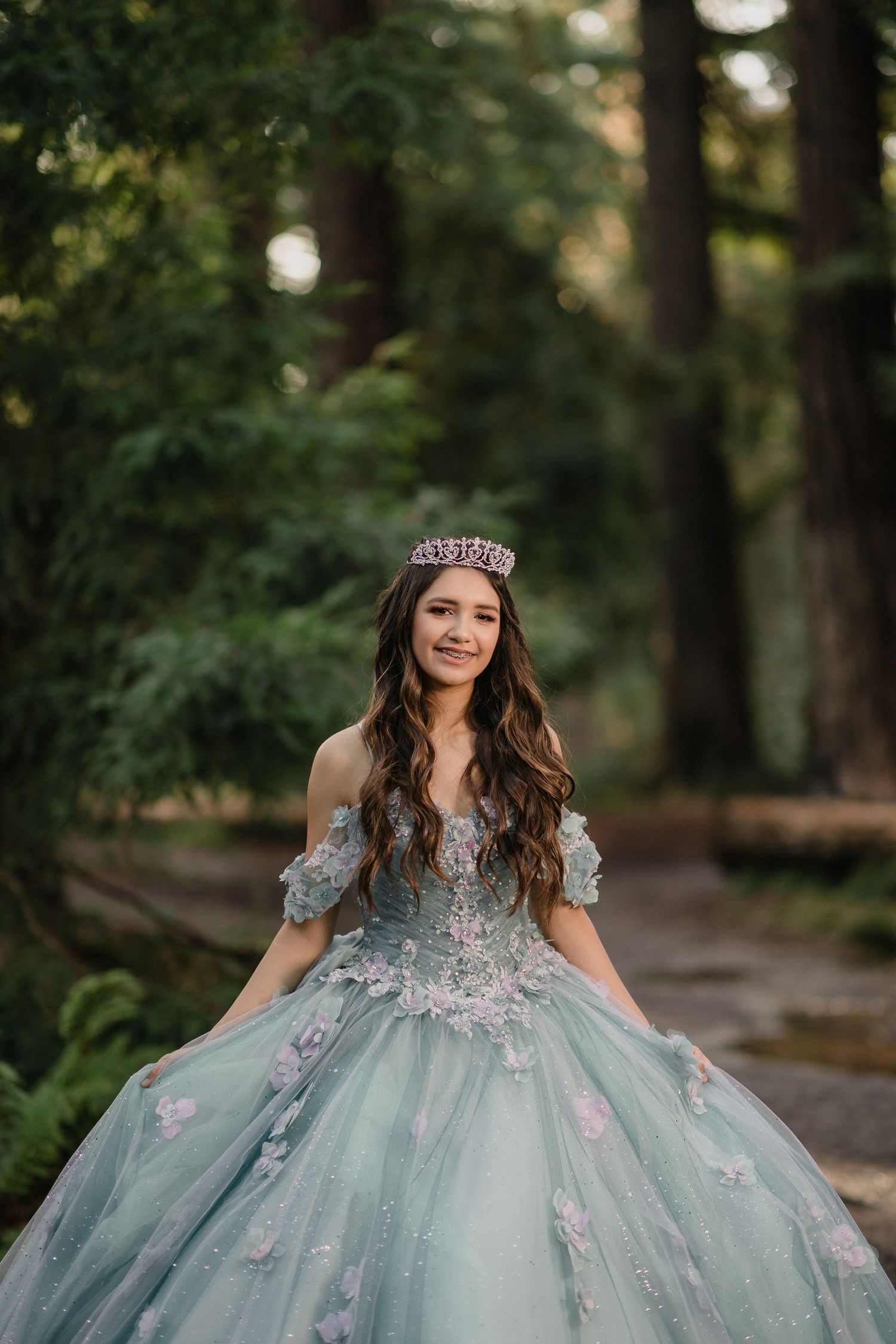 Enchanting forest portrait of person wearing crystal crown and powder blue ball gown with floral details.