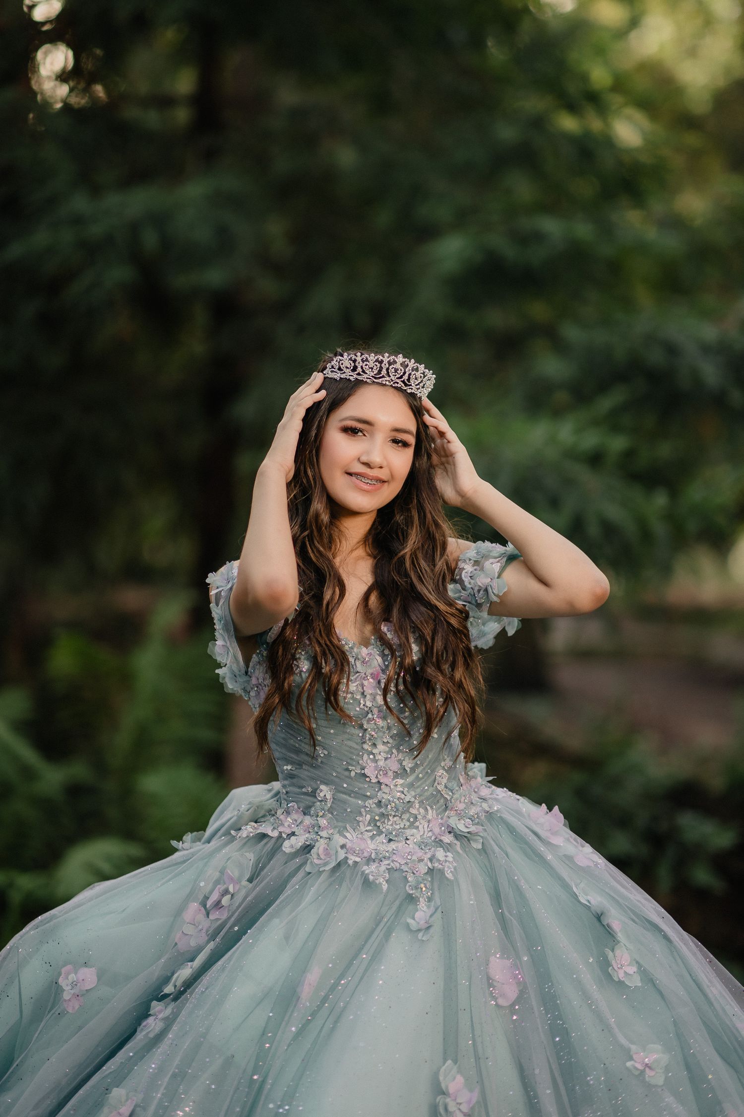 A fairytale-inspired photoshoot featuring a blue ball gown with floral appliques and a crystal crown in a forest setting.