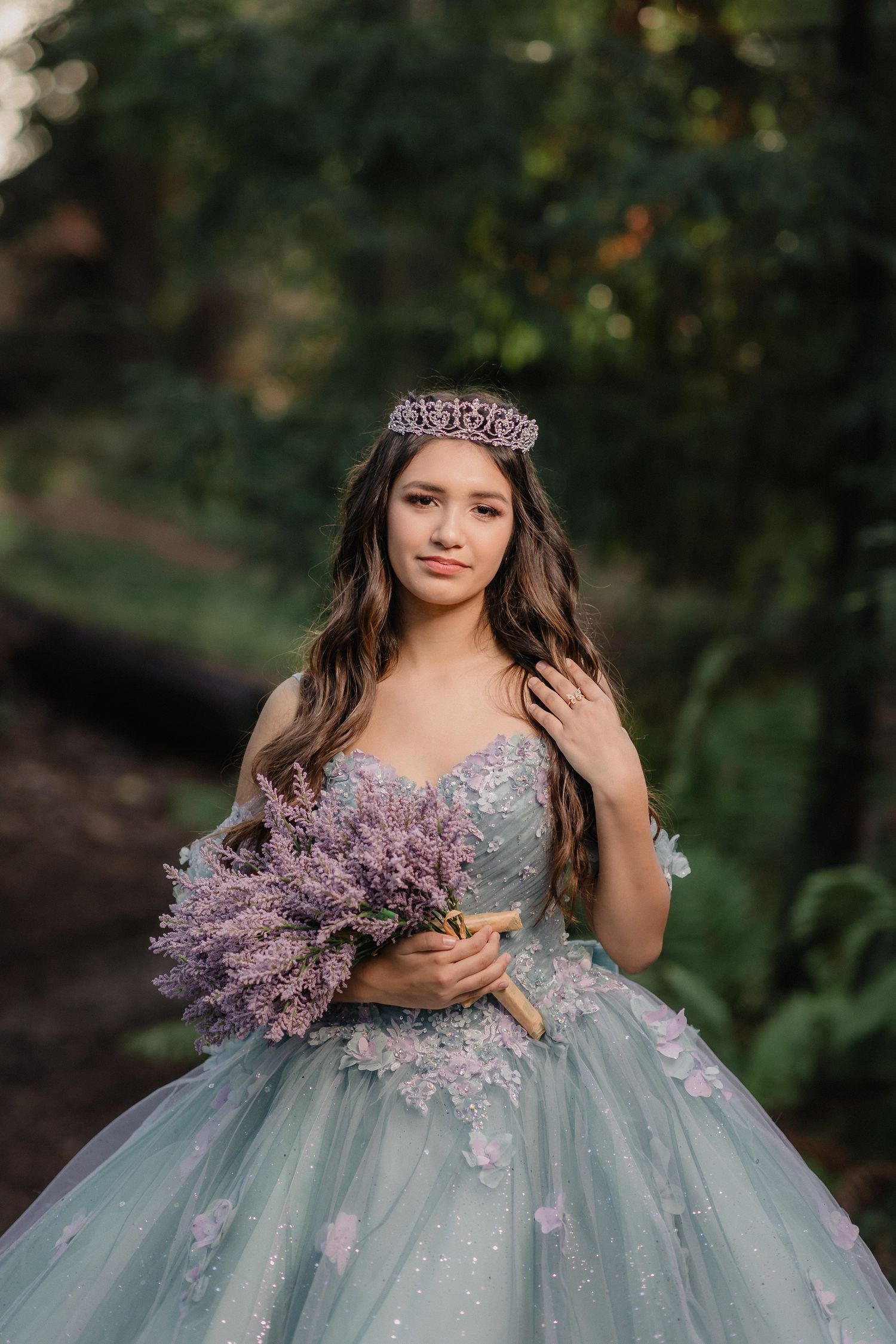 Dreamy portrait showcasing a blue tulle gown with lavender flowers and a tiara in a garden setting.